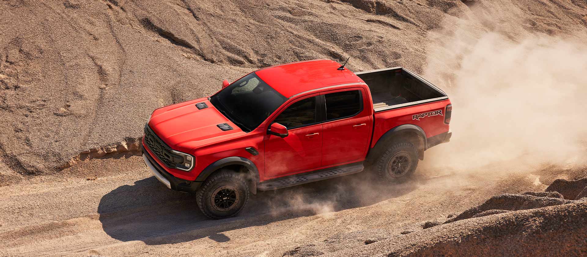 Ford Ranger Raptor orange grimpant une pente dans un nuage de poussière.