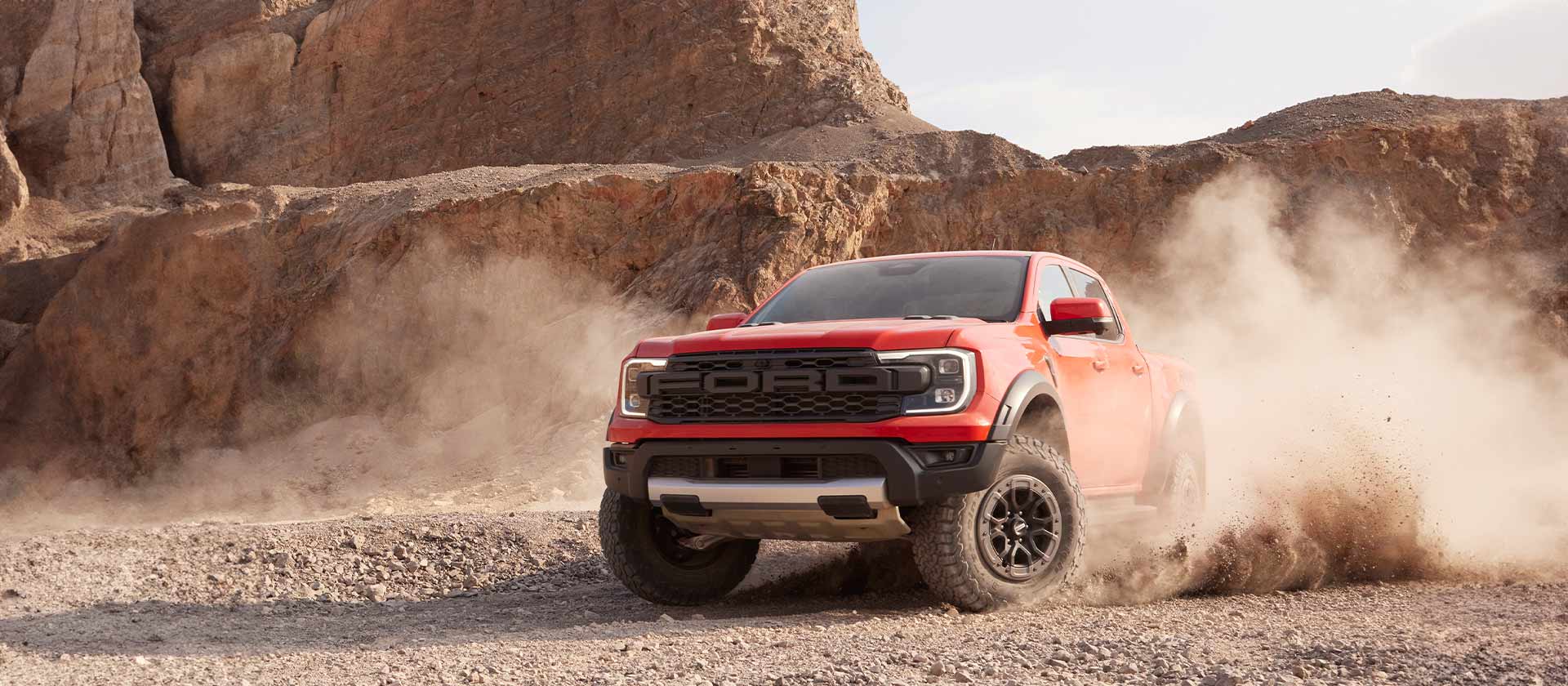 Ford Ranger Raptor orange roulant dans la poussière de roche concassée.
