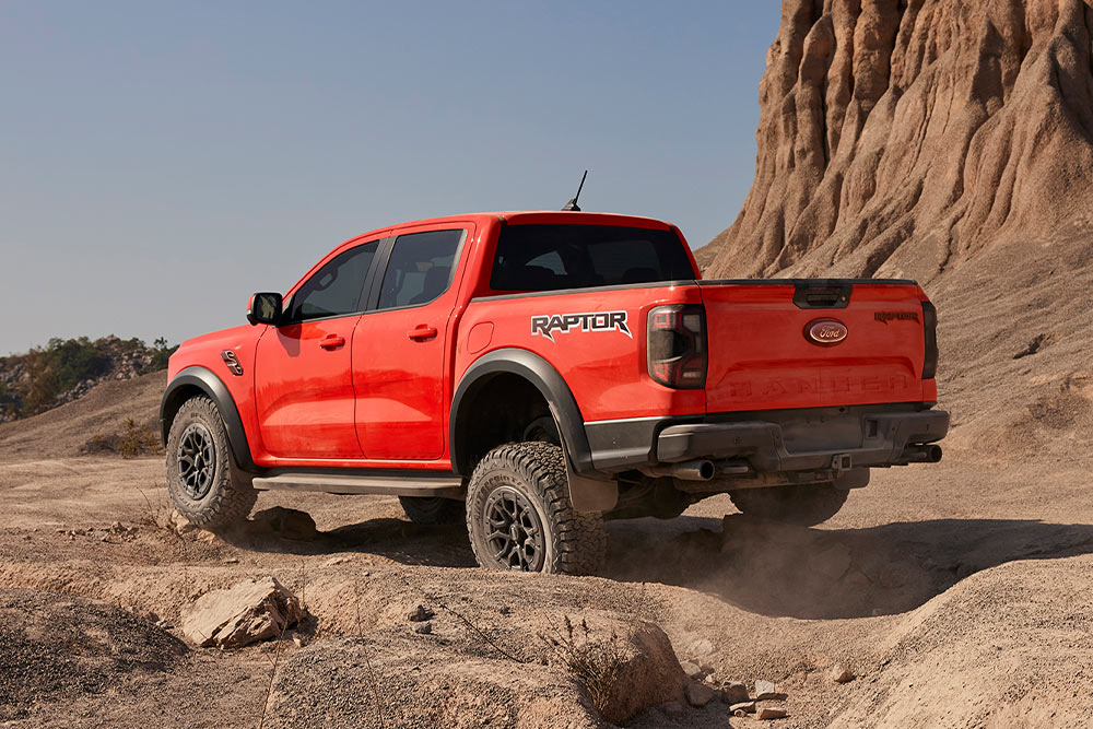 Ford Ranger Raptor en couleur Code Orange en montée tout-terrain sur des rochers.