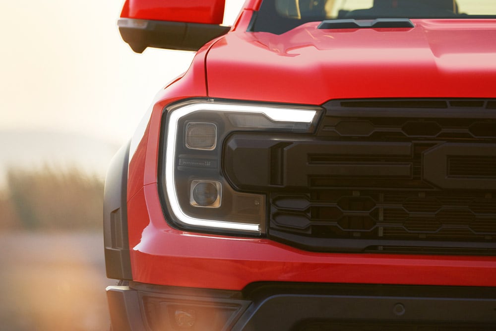 Gros plan sur le phare et la calandre d’un Ford Ranger Raptor en couleur Code Orange.