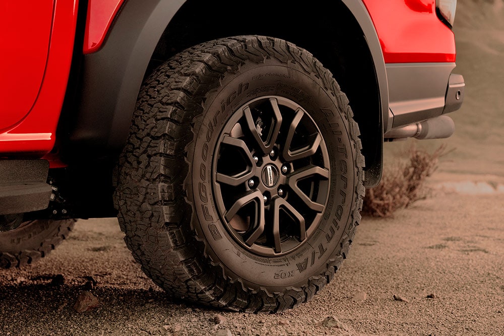 Ford Ranger Raptor en couleur Code Orange en montée tout-terrain sur des rochers.