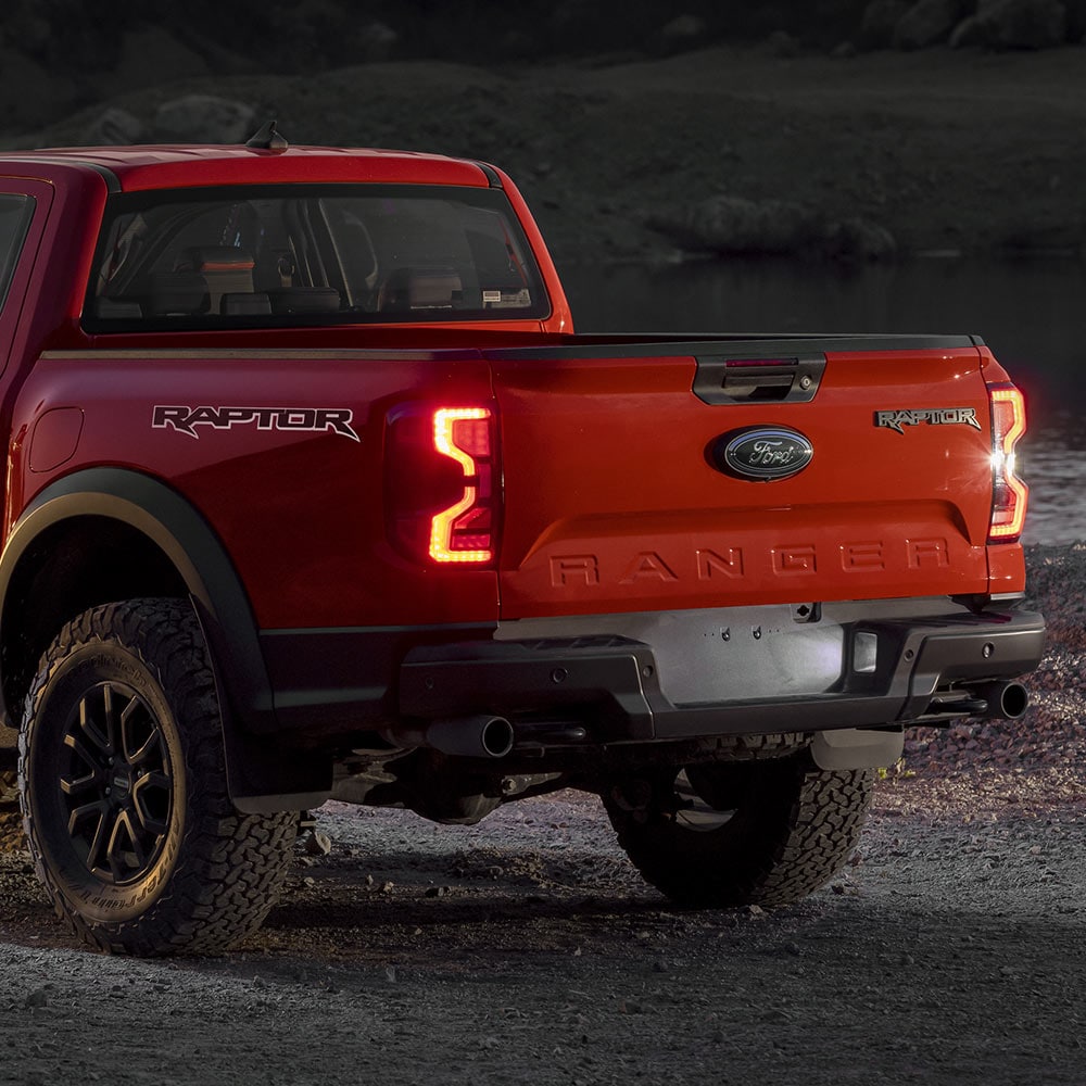 Vue arrière du Ford Ranger Raptor en couleur Code Orange, feux allumés.
