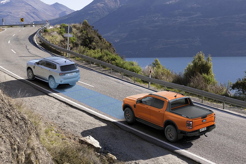 Un Ford Ranger Raptor jaune roulant sur une route de montagne pittoresque, mettant en avant ses systèmes d'aide à la conduite.