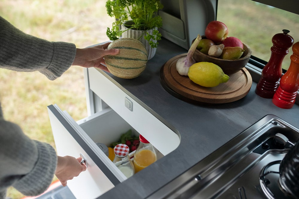 Réfrigérateur tiroir intégré de 33 litres dans le Ford Transit Custom Nugget, avec des fruits posés sur le plan de travail. 