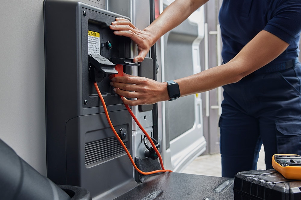 Gros plan d’une personne branchant un câble de recharge à l’intérieur d’un fourgon électrique Ford E‑Transit.