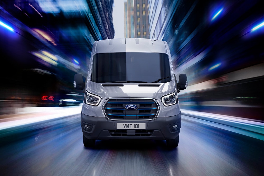 Vue de face d'un Ford Transit gris roulant à vive allure dans une ville la nuit