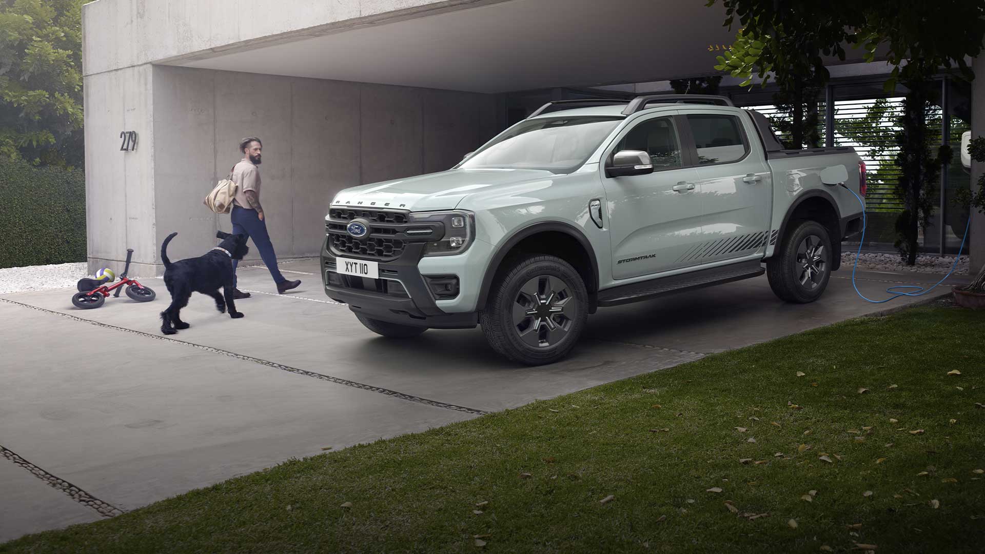 Un homme et un chien marchent vers un pick-up Ford Ranger Plug-in Hybrid gris en train de se recharger dans une allée.