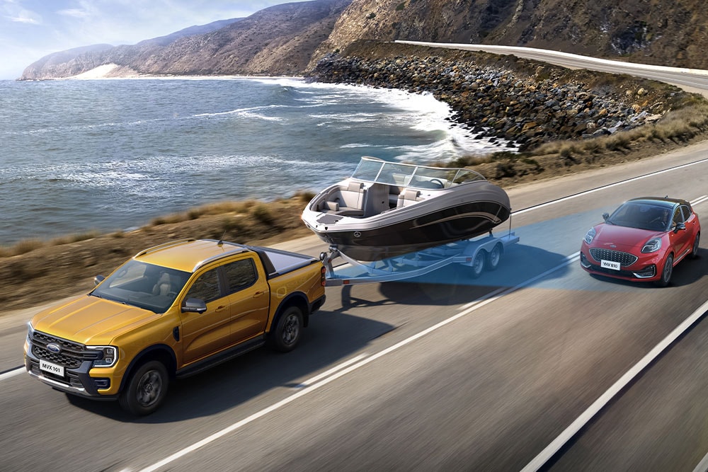 Un Ford Ranger jaune remorque un bateau le long d'une autoroute côtière, démontrant sa capacité de remorquage.