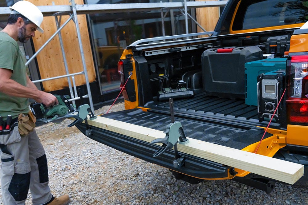 Le hayon d'un Ford Ranger jaune est abaissé, avec une planche de bois fixée dessus à l'aide d'une pince.