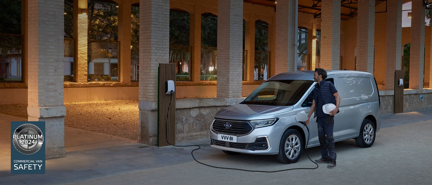 Un homme qui tient un casque de sécurité branche un câble de chargement d’un boîtier mural dans le nouveau Ford Transit Connect en Stardust Silver.