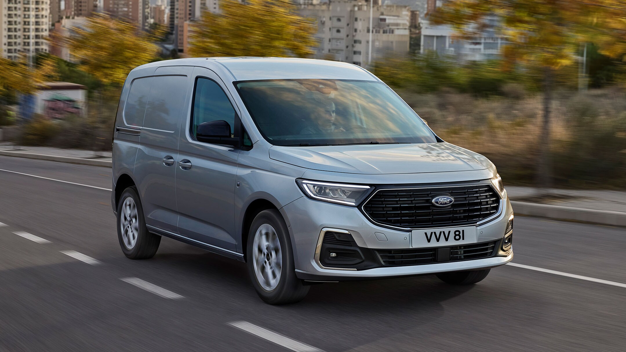 Le nouveau Ford Transit Connect Limited en Stardust Silver roule sur une route. Il est équipé de contours extérieurs chromés et de phares automatiques.