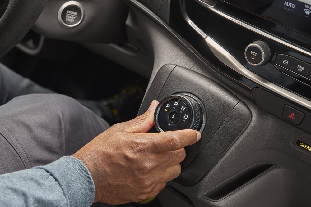 Main actionnant le sélecteur rotatif de vitesses sur la console centrale d’un fourgon Ford Transit. 