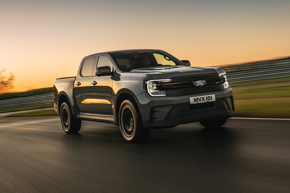 Un Ford Ranger Platinum gris foncé roule sur une piste au coucher de soleil.