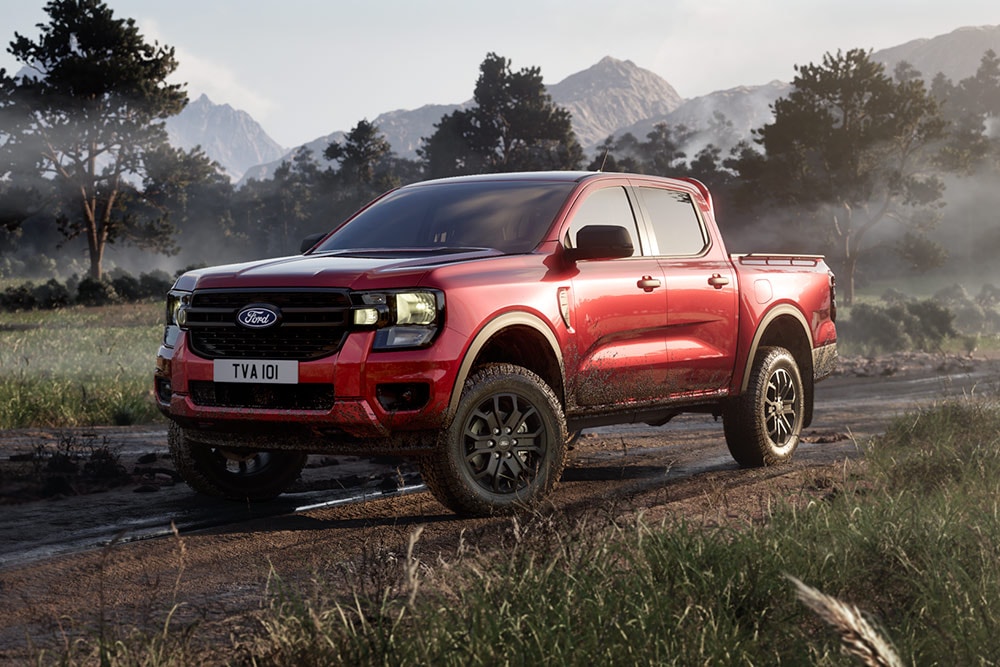 Un Ford Ranger Raptor rouge roulant sur un chemin de terre à travers un paysage pittoresque.