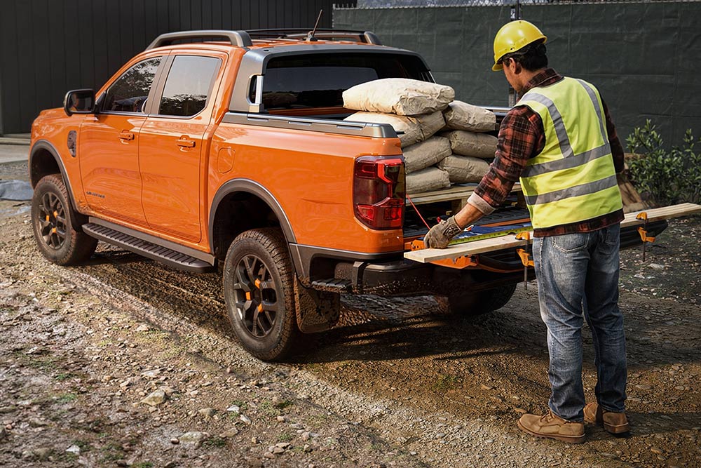 Un ouvrier du bâtiment charge du matériel sur la plateforme d’un Ford Ranger orange.