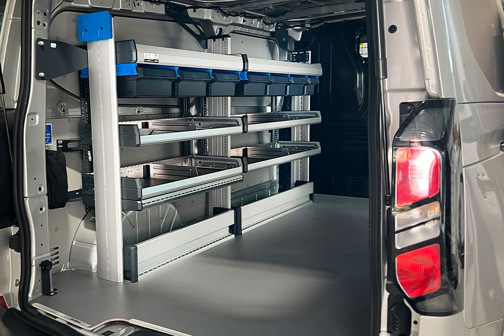 Intérieur arrière d'une camionnette Ford Transit, montrant un système d'étagères modulaires avec divers bacs de rangement.