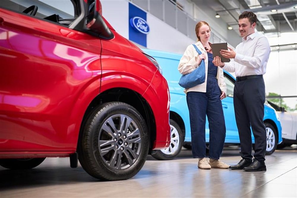 Une mécanicienne Ford intervenant sur le pneu avant d’une voiture verte, tandis qu’un autre technicien déplace un pneu. 