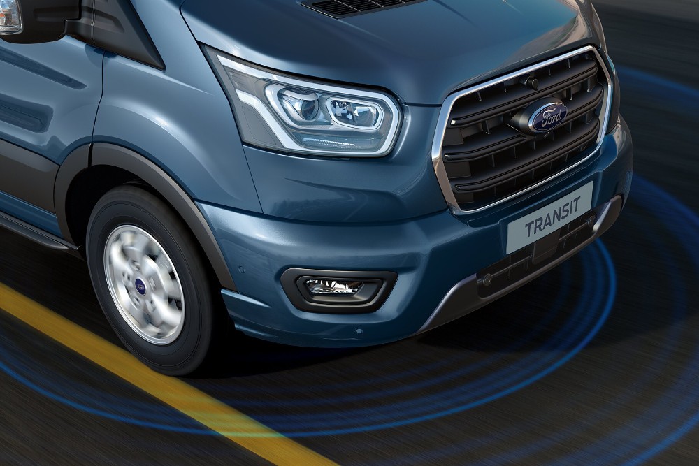 Vue de l'angle avant d'une fourgonnette Ford Transit bleue, avec les anneaux des capteurs de stationnement visibles au sol.